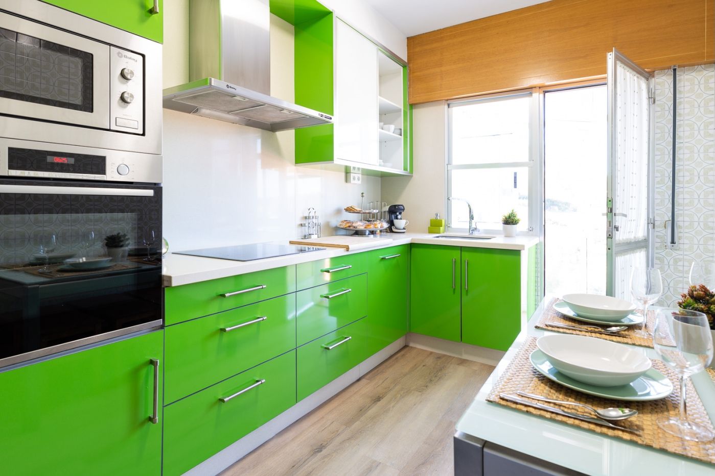 Une cuisine moderne avec des meubles de couleur verte, un four encastré et une fenêtre qui laisse entrer la lumière naturelle.