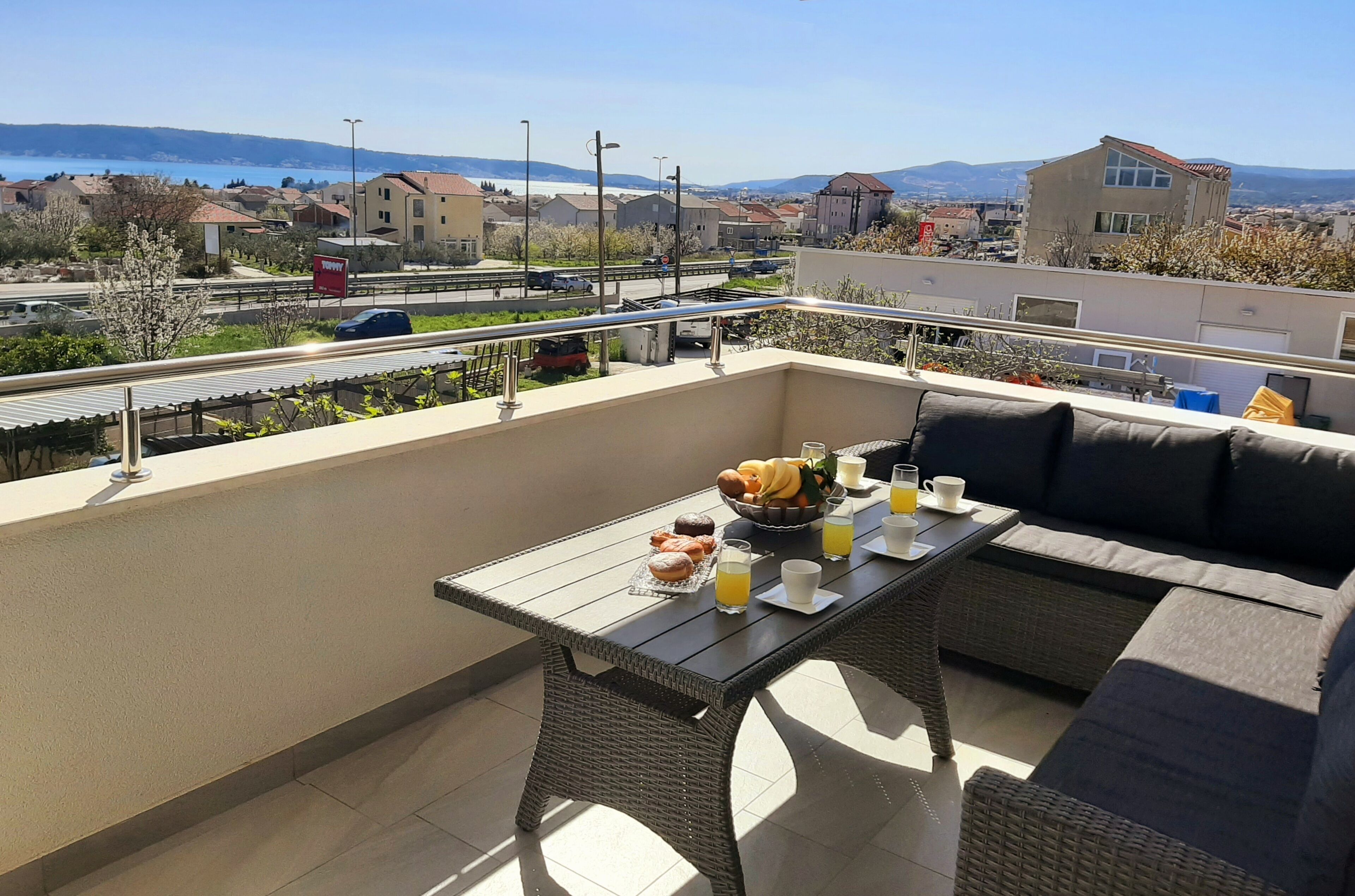Un balcon avec une table préparée pour le petit-déjeuner, des meubles en osier et une vue sur la ville et les montagnes.