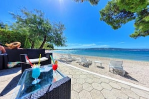 Un patio frente a la playa con una mesa de vidrio, sillas de descanso y vistas al mar.