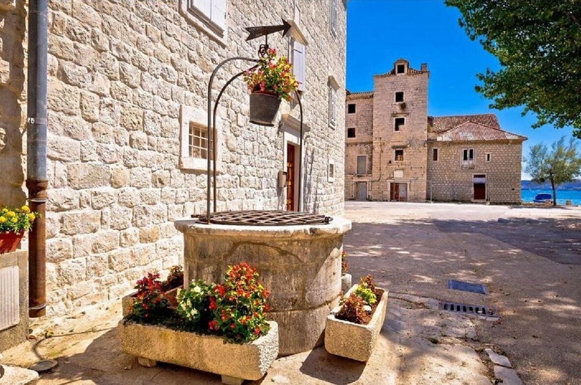 A stone building with a well, flower pots, and a clear view of the sea.
