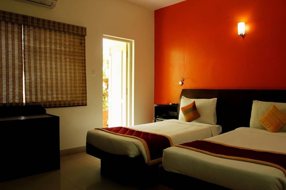 A hotel room with two beds, a nightstand, a desk, and a window with blinds.