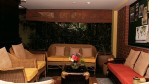 A cozy lounge area with wicker furniture, a coffee table with a vase of flowers, and a brick wall with a bulletin board. - The Green Path (Bengaluru)