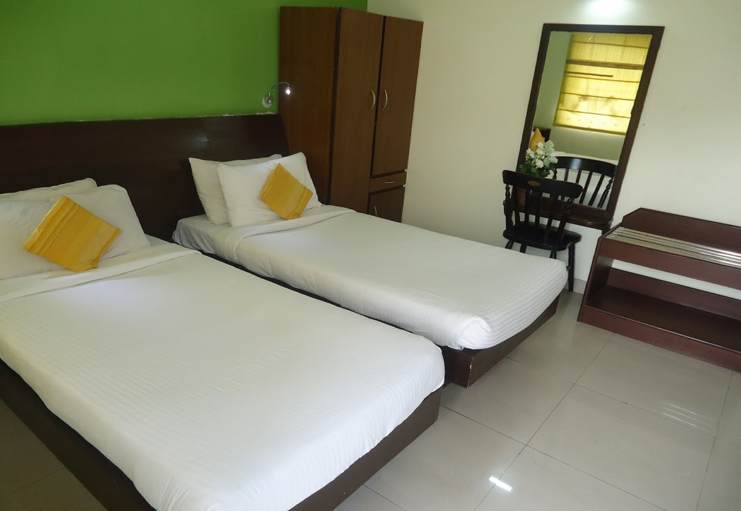 A room with two single beds, a wooden wardrobe, a desk with a chair, and a mirror.
