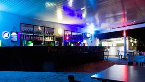 Una zona de bar con barra, estanterías llenas de botellas y un área de estar con mesas y sillas.