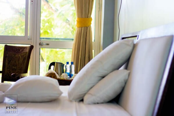 A hotel room with a bed, pillows, a chair, a nightstand with water bottles, and a window with curtains. - Pine Court Malindi (Malindi)