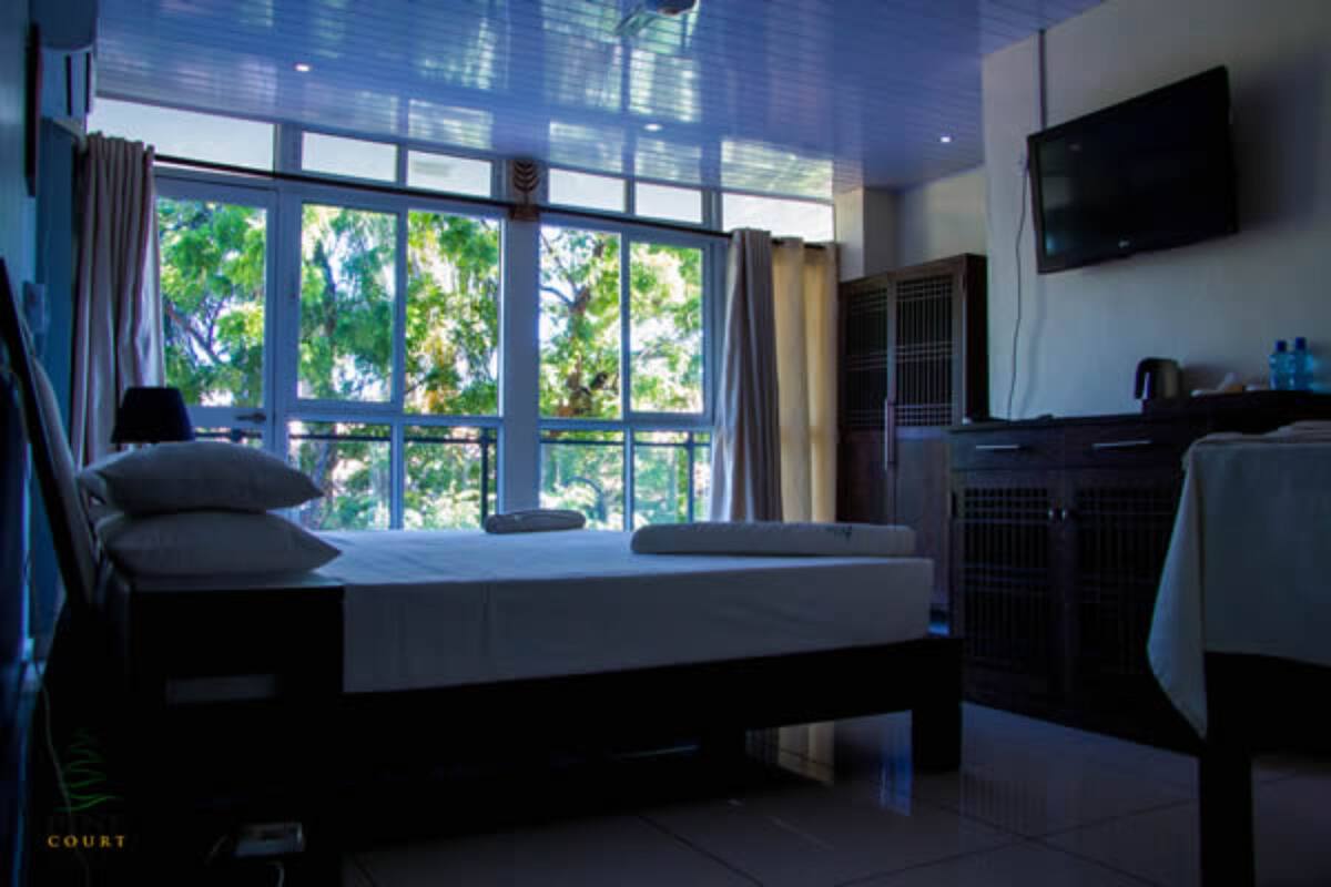 Quarto com cama, televisão, escrivaninha e janela com vista para árvores.