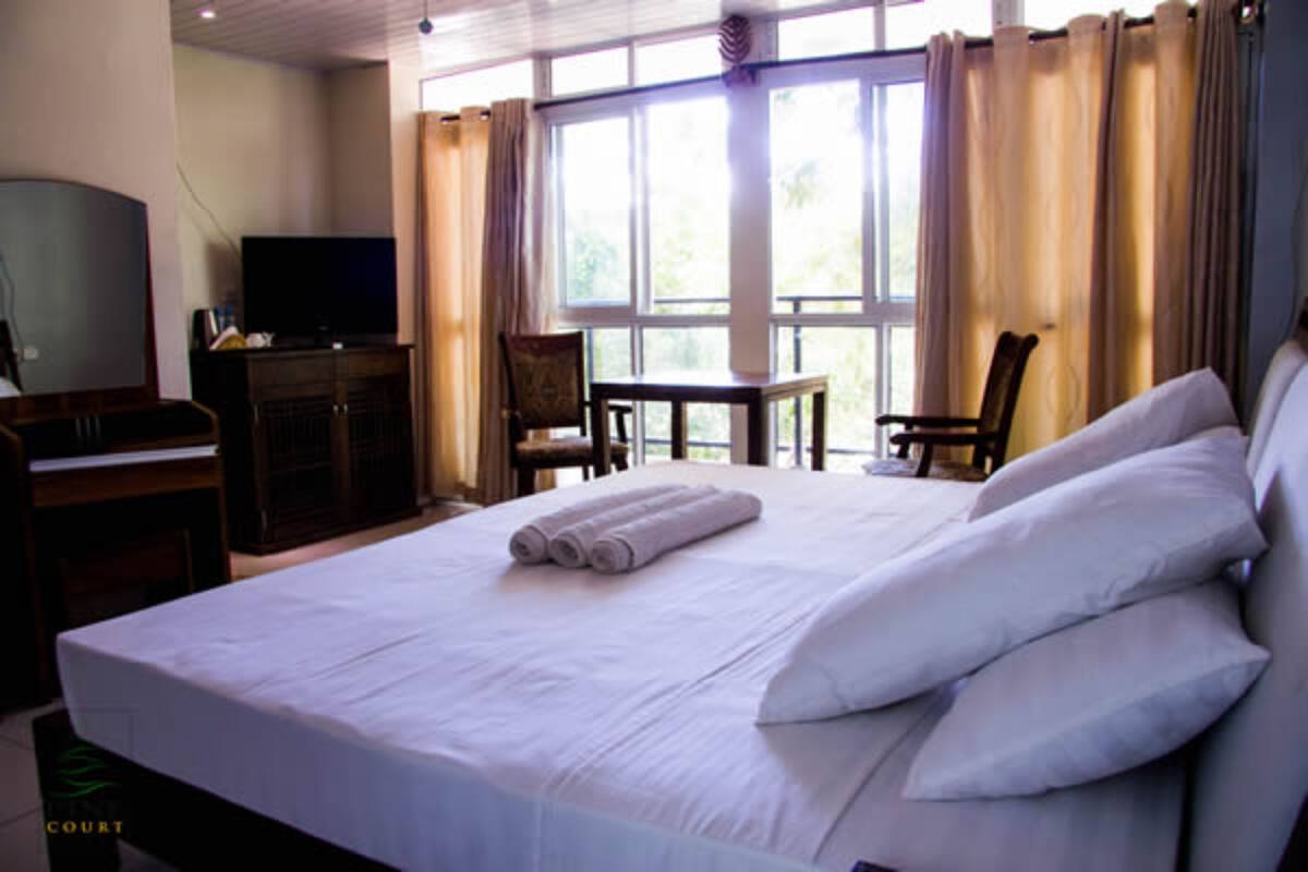 Quarto de hotel com uma cama grande, uma mesa de trabalho com televisão e vista para o exterior através de grandes janelas.