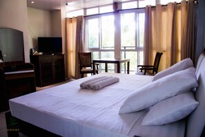 A hotel room with a large bed, a desk with a television, and a view of the outdoors through large windows. - Pine Court Malindi (Malindi)