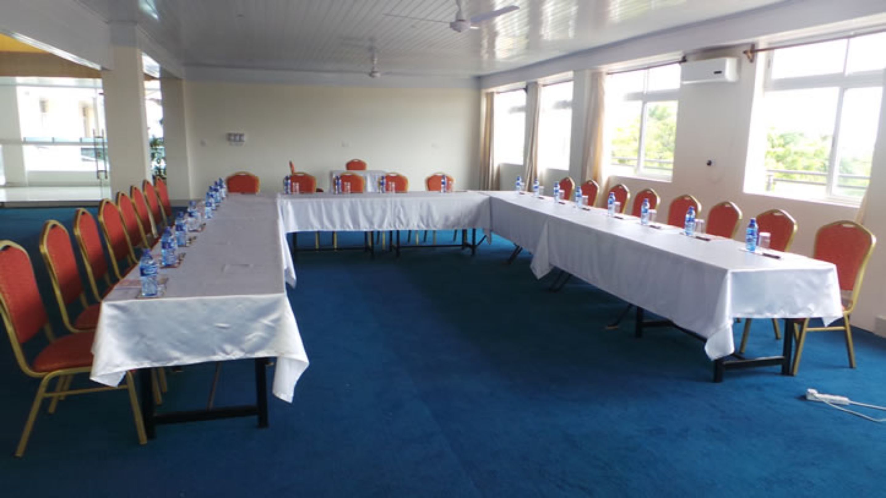 Une salle de conférence avec une longue table, des chaises rouges et des nappes blanches.