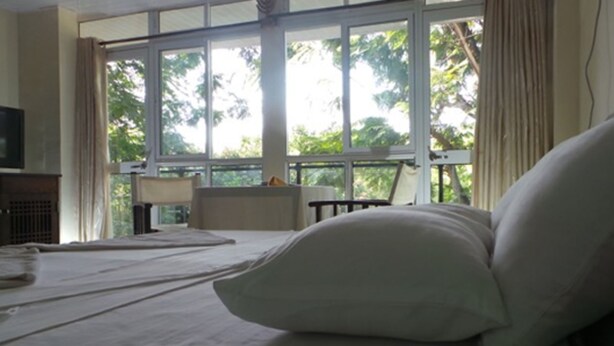Habitación de hotel con cama, televisor, ventana con cortinas y vista a zonas verdes.