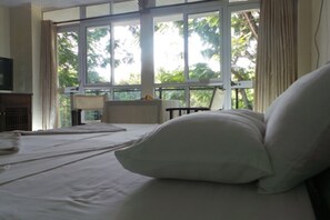 A hotel room with a bed, a television, a window with curtains, and a view of greenery outside. - Pine Court Malindi (Malindi)