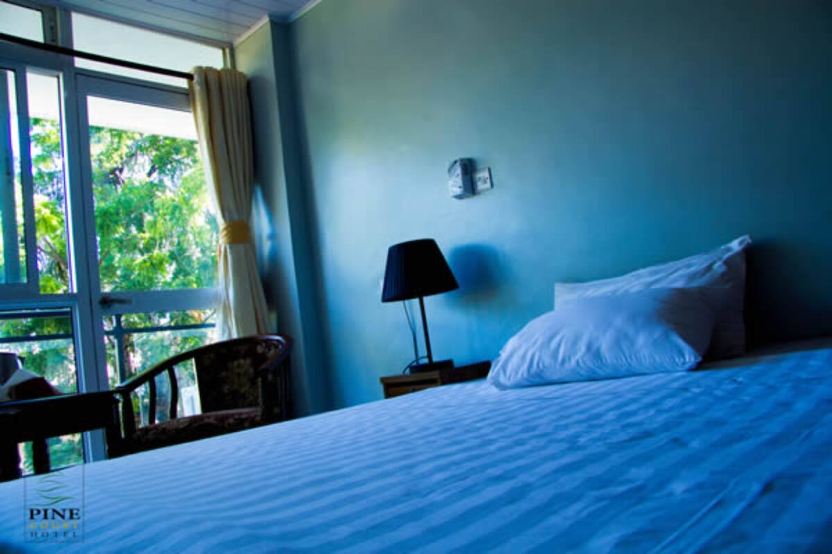 Quarto com cama, cadeira, mesa de cabeceira com abajur e janela com cortinas.