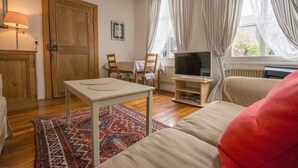 Un salon confortable avec un canapé, un téléviseur, une porte en bois et un tapis à motifs.