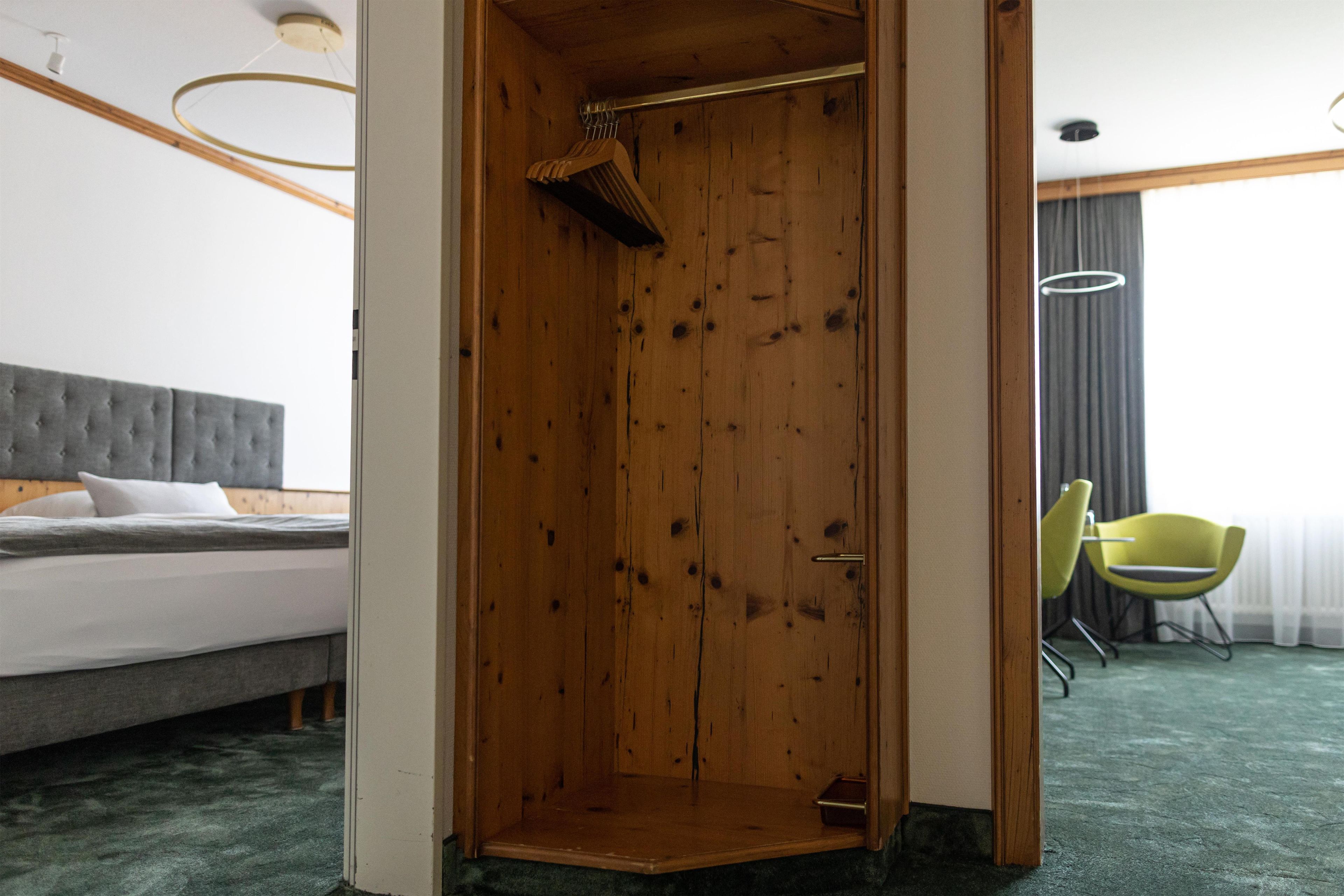 A hotel room with a wooden wardrobe, a bed with grey bedding, a green carpet, and a yellow chair.