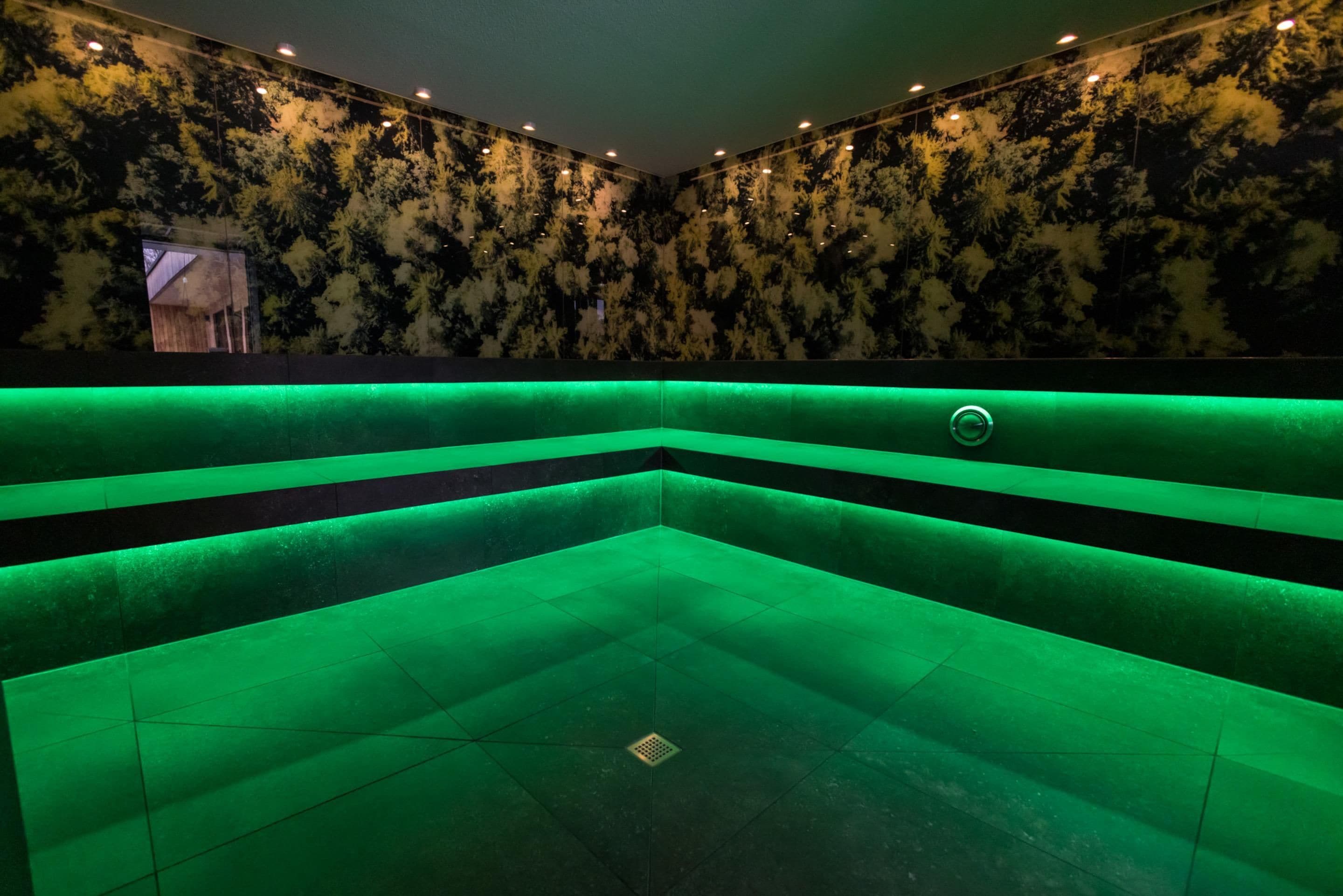 Een kamer met een badkuip verlicht in het groen, een behang met patroon en inbouwspots.