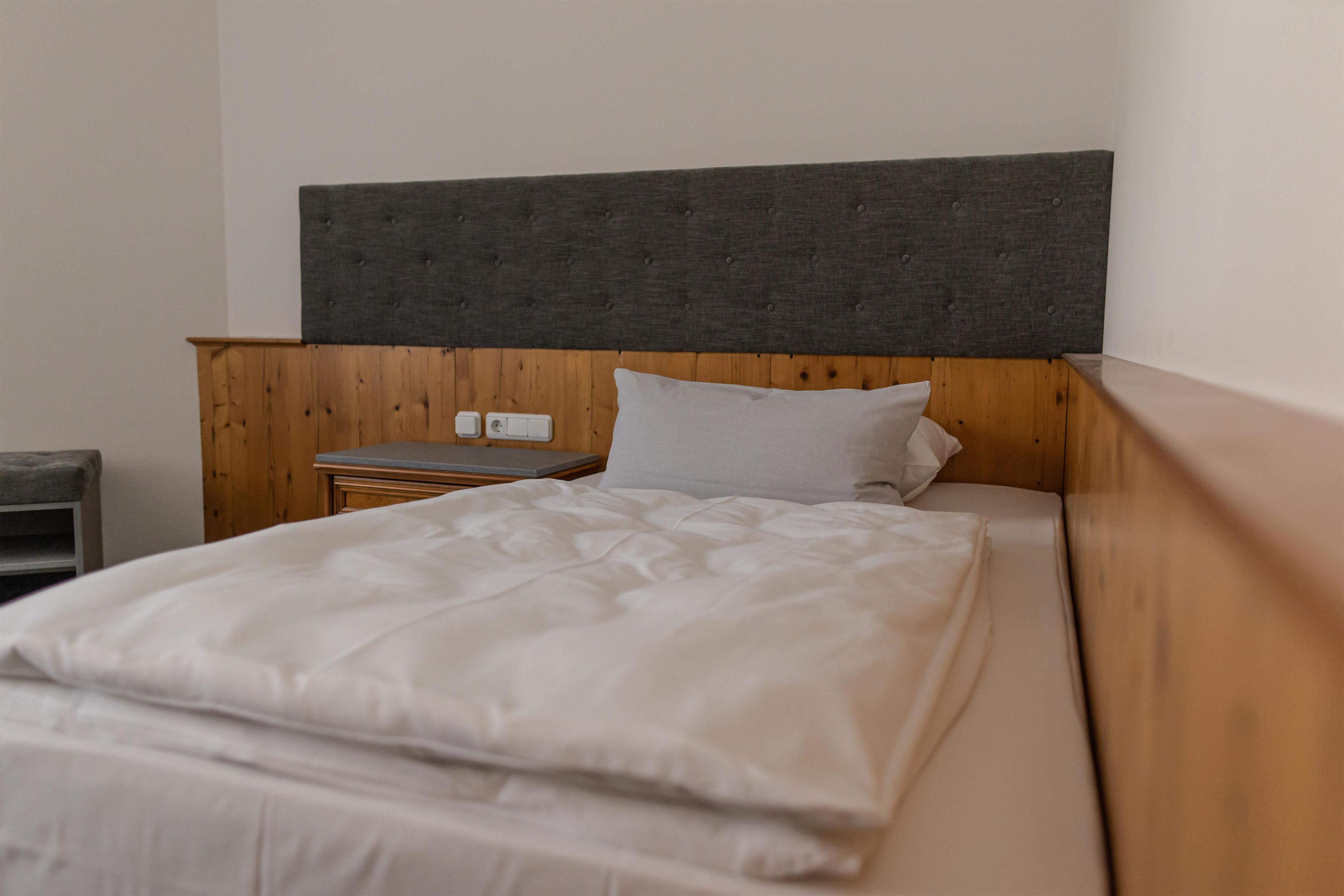 Een eenpersoonsbed met een houten hoofdbord, een nachtkastje en een bedtafel.