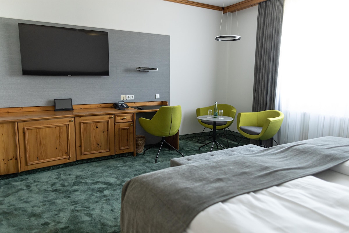 A hotel room with a bed, a desk with a computer, a TV mounted on the wall, and two chairs.