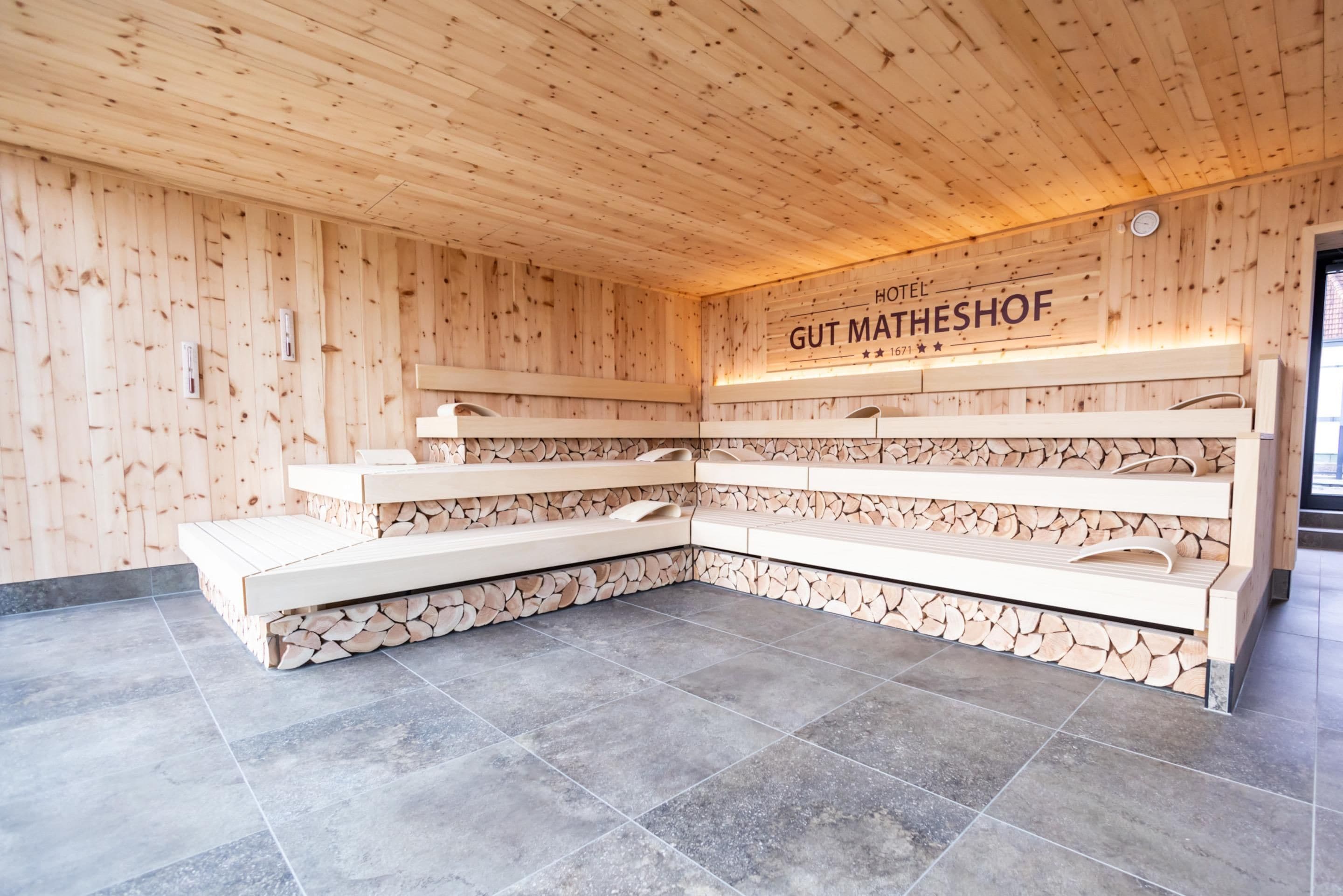 A sauna room with wooden walls and a tiled floor, featuring a bench and shelves for towels.