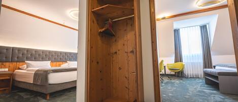 Habitación de hotel con cama, armario de madera, zona de estar con una silla y una mesa, y vistas al exterior a través de una ventana.