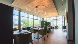 Un comedor moderno con suelo de madera, sillas verdes y grandes ventanales con vistas al exterior.