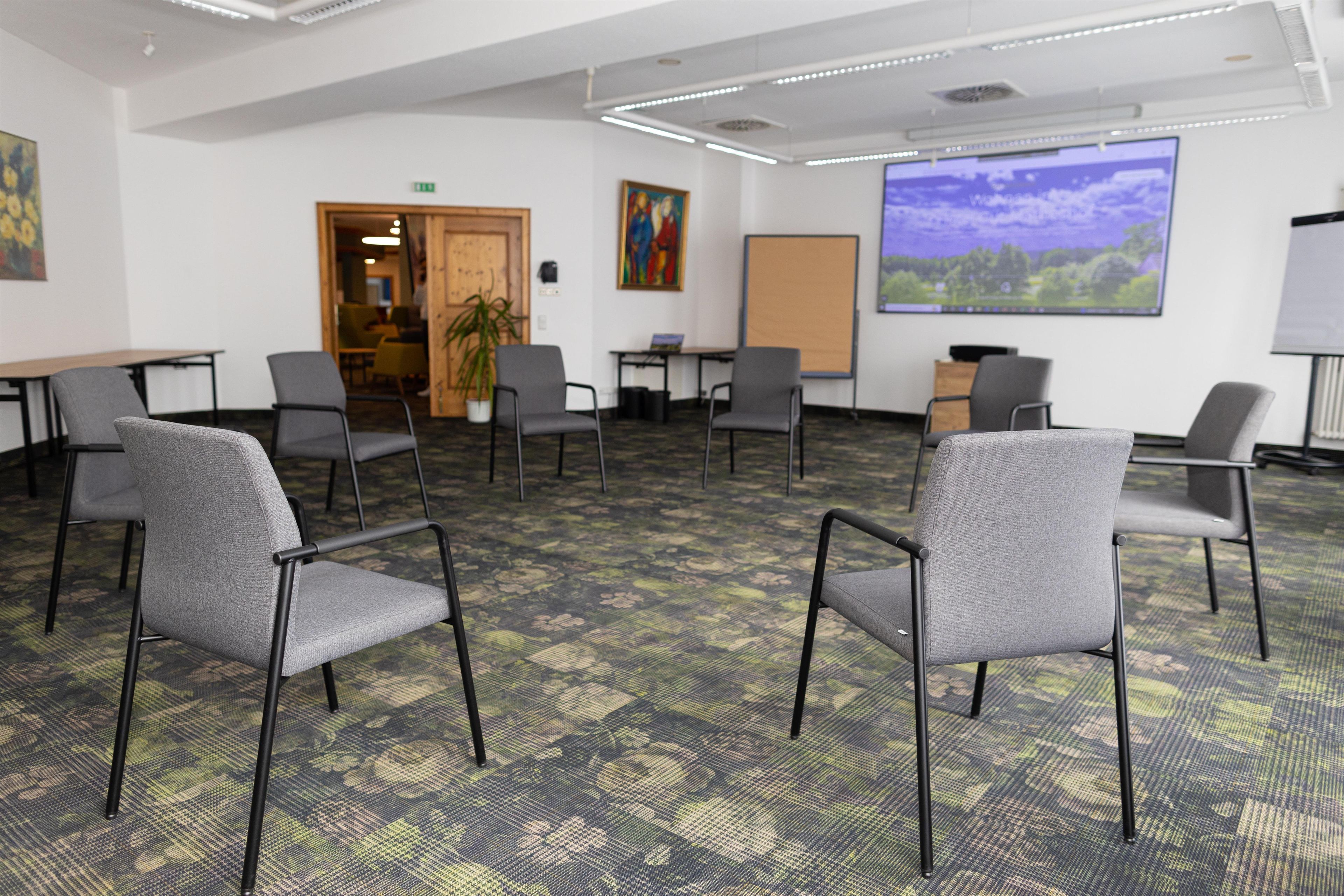 A conference room with a carpeted floor, grey chairs, a whiteboard, and a projector screen displaying a landscape.