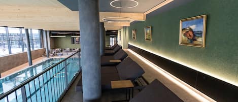 Un interior moderno con barandilla de cristal que da a una piscina, zonas de estar y obras de arte en las paredes.