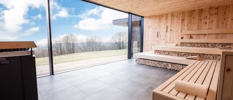 Un interior moderno con techo de madera, ventanas grandes y vista a un paisaje cubierto de hierba.