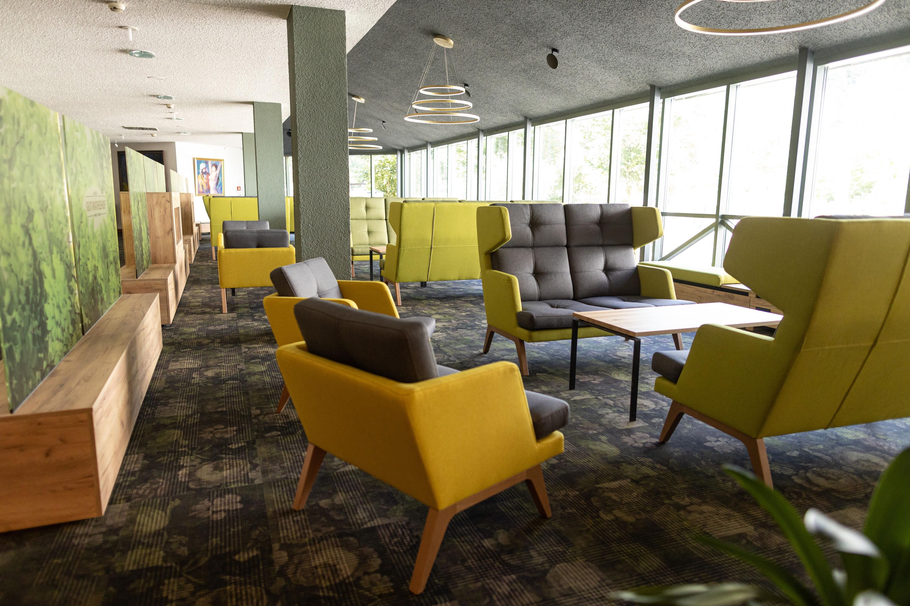 A modern indoor seating area with yellow and grey chairs, a wooden table, and a patterned carpet.