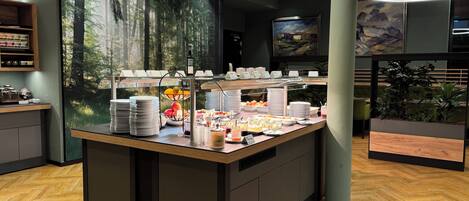 A breakfast bar with a variety of food items, a coffee station, and a large mural of a forest.