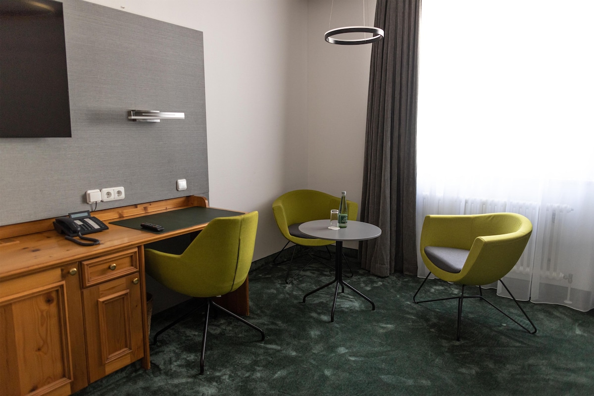 A hotel room with a desk, two chairs, a small table, a telephone, and a wall-mounted light fixture.