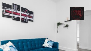 Un salon moderne avec un canapé bleu, une table basse en bois et des œuvres d’art abstraites accrochées au mur.