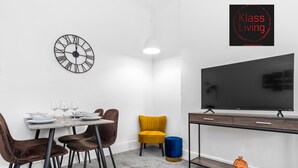 Un salon moderne avec un coin repas, comprenant un grand téléviseur à écran plat, une horloge murale et un canapé.