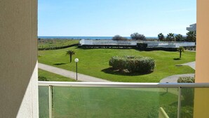 A balcony with a view of a well-maintained lawn, a pathway, and a distant building. - Seaside Apartment with Pool, Parking, and Pets Allowed (Saint-Cyprien)