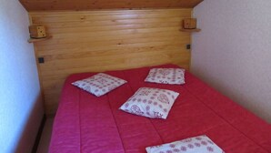 Una habitación pequeña y estrecha con techo inclinado de madera, una cama individual con colchón rojo y almohadas estampadas.