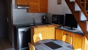 Una cocina compacta con armarios de madera, lavavajillas, microondas y una mesa de comedor con sillas.