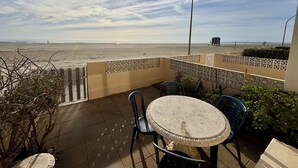 A patio with a table and chairs, a view of the beach, and a street lamp.