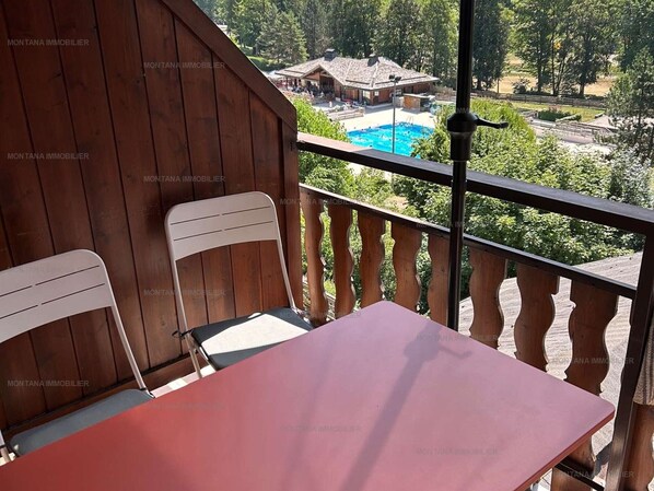 A balcony with a wooden railing, a table, and two chairs.