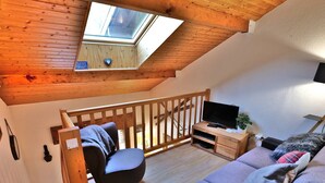 A cozy loft bedroom with a skylight, wooden staircase, a TV, and a sofa. - Charming 2-Room Mezzanine Apt in Grand-Bornand Village, Sleeps 4, Balcony, Steps from Ski Lifts (Le Grand-Bornand)