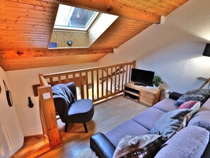 A cozy loft bedroom with a skylight, wooden staircase, a TV, and a sofa.