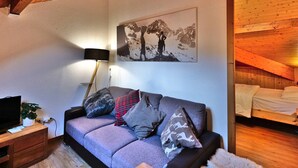 A cozy room with a wooden ceiling, a sofa with patterned cushions, a mounted picture, and a bedside table with a lamp. - Charming 2-Room Mezzanine Apt in Grand-Bornand Village, Sleeps 4, Balcony, Steps from Ski Lifts (Le Grand-Bornand)