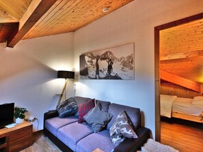 Ein gemütliches Zimmer mit Holzboden, einer Couch mit gemusterten Kissen, einem Wandbild und einem Nachttisch mit Lampe.