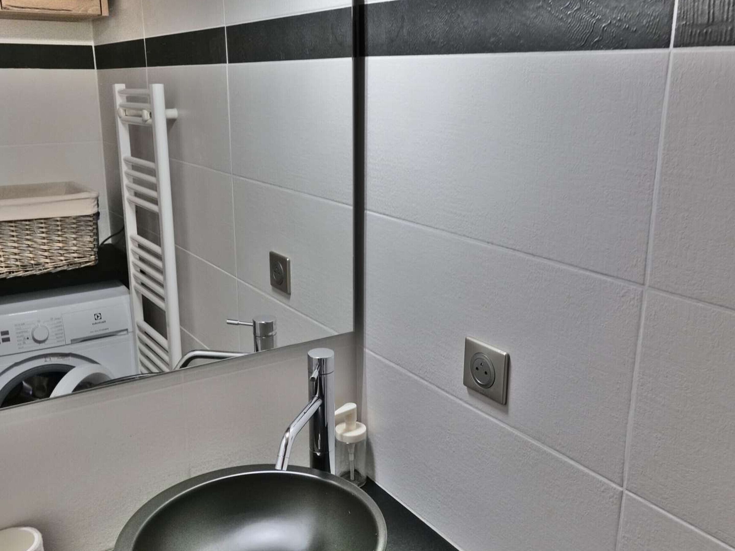 A modern bathroom with a large mirror, a sink, and a washing machine in the background.