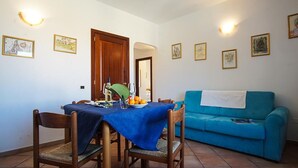 A dining area with a table set for two, a blue sofa, and artwork on the walls.