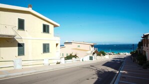 A coastal street with buildings, a clear blue sky, and the sea in the background.