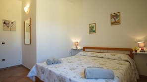 Quarto com cama, duas mesinhas de cabeceira, um criado-mudo e uma obra de arte na parede.