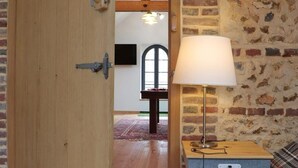 An open wooden door leading to a room with a brick wall, a lamp, and a small table with a box.
