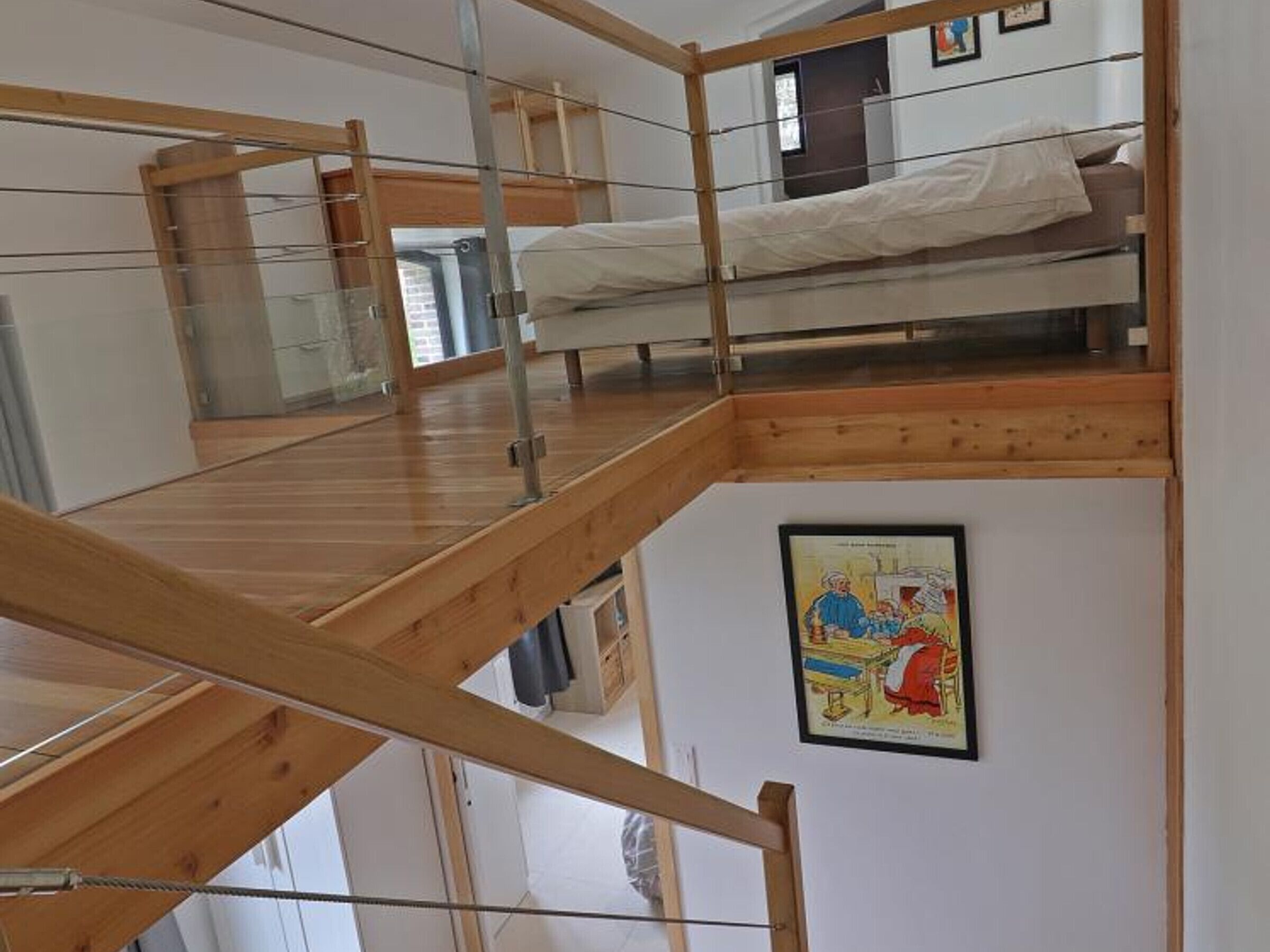 Habitación con literas de madera en varios niveles, barandilla de cristal y un cuadro en la pared.