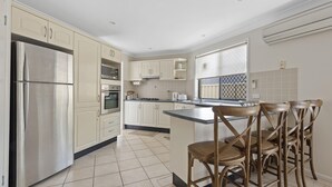 Una cocina moderna con electrodomésticos de acero inoxidable, armarios blancos y una zona de bar con sillas de madera.