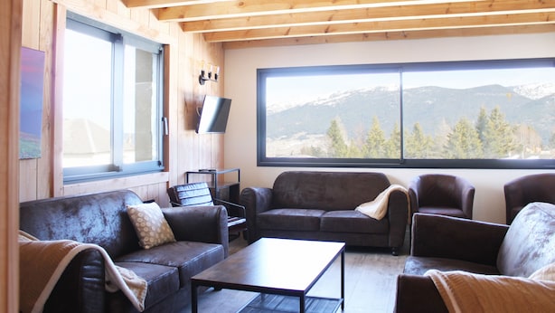 Un salon chaleureux avec des poutres en bois, une grande fenêtre donnant sur les montagnes et des canapés en cuir.