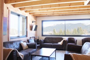 Un salon chaleureux avec des poutres en bois, une grande fenêtre donnant sur les montagnes et des canapés en cuir.